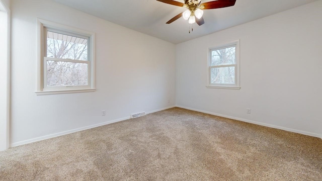 carpeted spare room featuring visible vents, baseboards, and ceiling fan