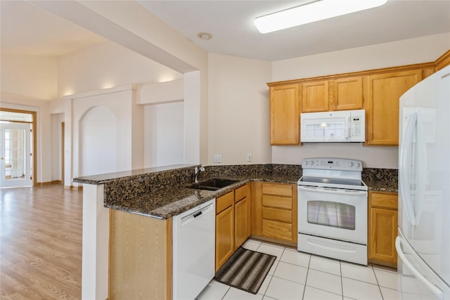 kitchen featuring white appliances, dark stone counters, a peninsula, a sink, and light tile patterned flooring