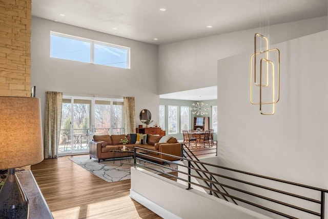 living room with a towering ceiling, an inviting chandelier, wood finished floors, and recessed lighting