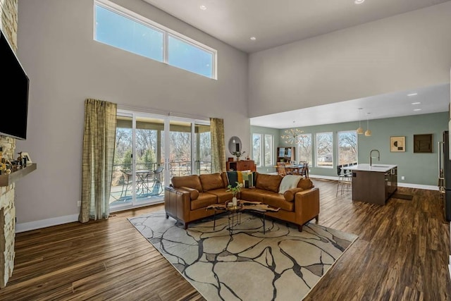 living room with a stone fireplace, recessed lighting, a high ceiling, dark wood-style flooring, and baseboards