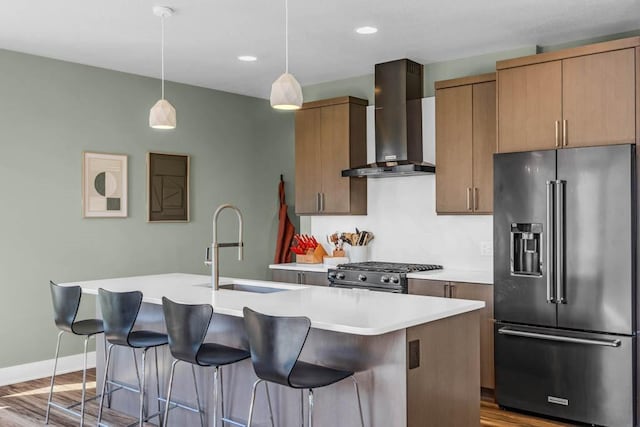 kitchen with high end appliances, a kitchen island with sink, a sink, and wall chimney exhaust hood