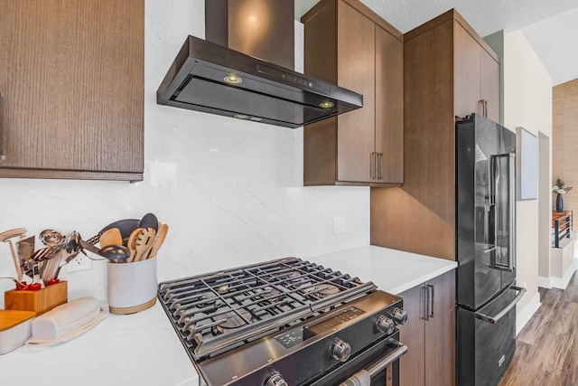 kitchen featuring light countertops, stainless steel range with gas stovetop, high end black fridge, wood finished floors, and wall chimney exhaust hood