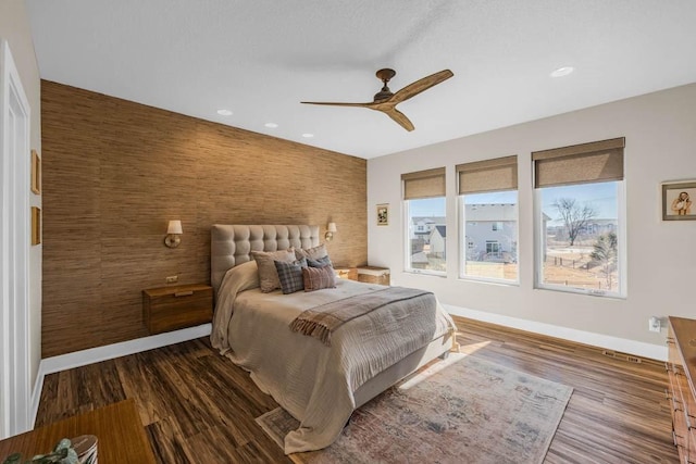 bedroom with dark wood-style floors, an accent wall, a ceiling fan, and baseboards