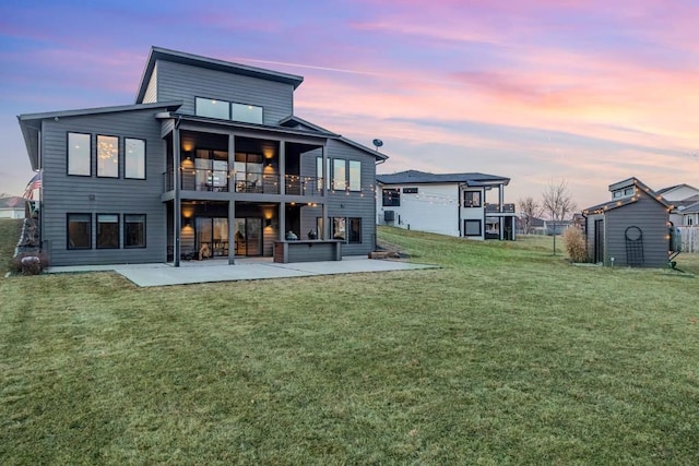 back of property at dusk with a patio, a lawn, a balcony, a shed, and an outdoor structure