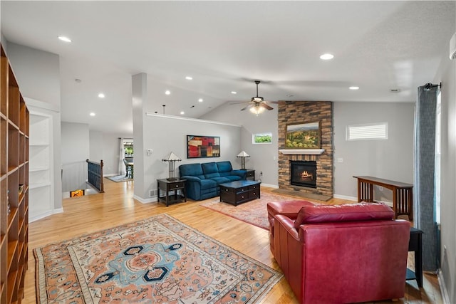 living room with baseboards, lofted ceiling, ceiling fan, a stone fireplace, and light wood-type flooring