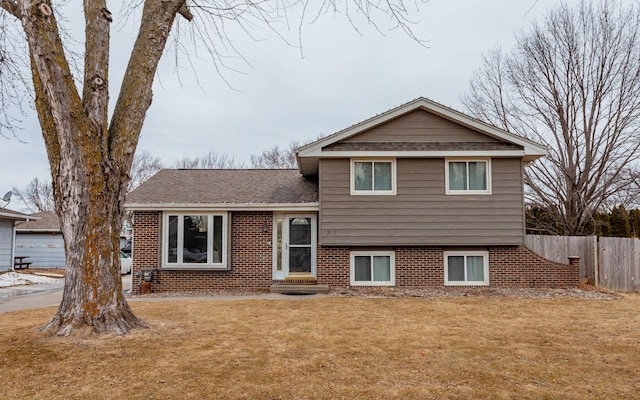 tri-level home featuring a shingled roof, fence, a front lawn, and brick siding