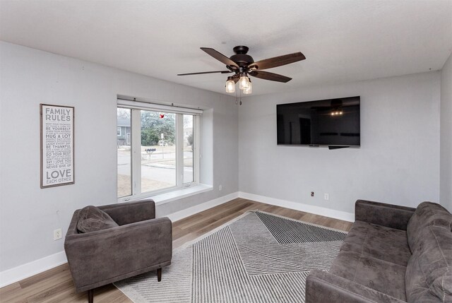 living area with a ceiling fan, baseboards, and wood finished floors