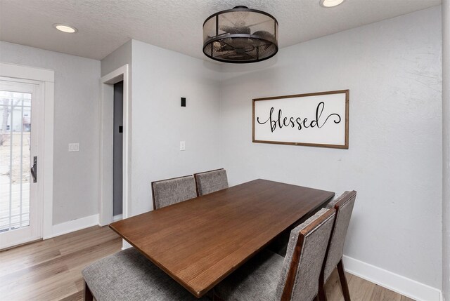 dining space featuring a textured ceiling, baseboards, and wood finished floors