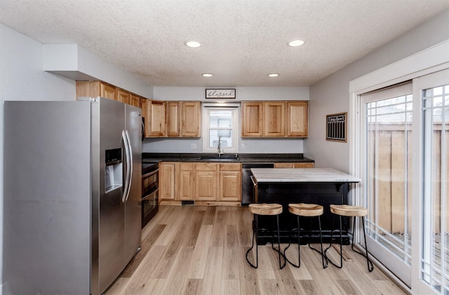 kitchen with range with two ovens, dishwasher, light wood-style floors, stainless steel refrigerator with ice dispenser, and a sink