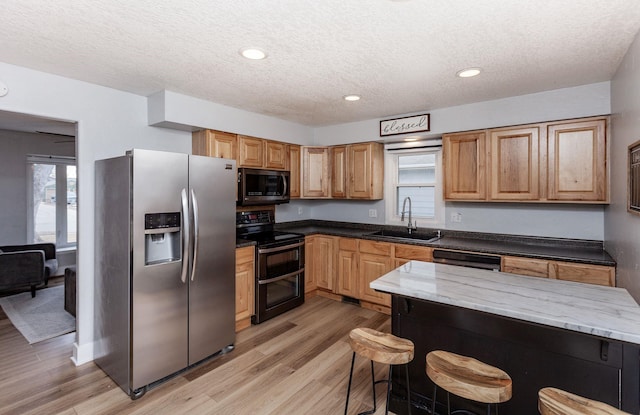 kitchen featuring stainless steel appliances, a sink, light wood-style flooring, and a breakfast bar area