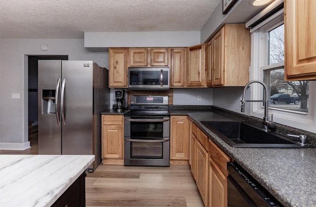 kitchen featuring a textured ceiling, appliances with stainless steel finishes, light wood-type flooring, and a sink