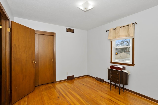 unfurnished bedroom featuring light wood-style flooring, visible vents, baseboards, and a closet