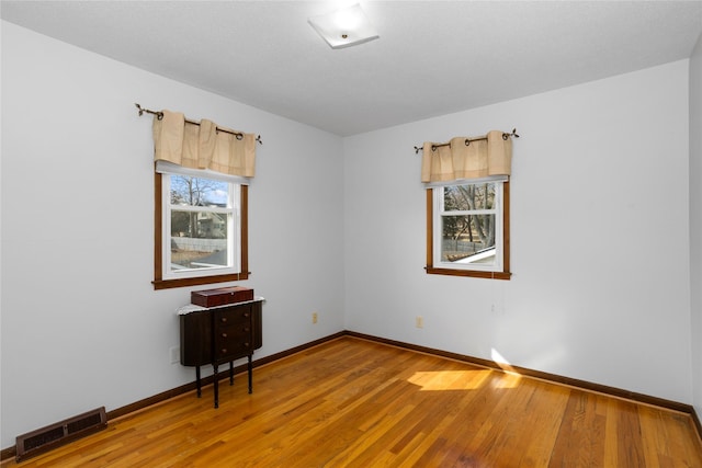 empty room with light wood-style floors, visible vents, and baseboards