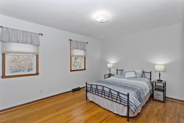 bedroom with multiple windows, baseboards, and wood finished floors