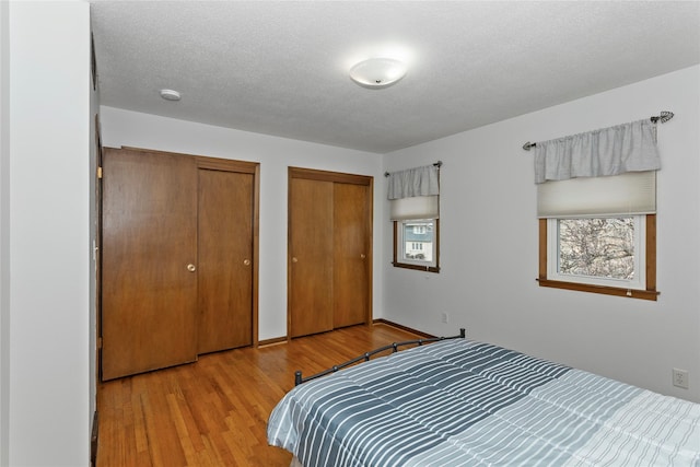 bedroom with a textured ceiling, wood finished floors, and multiple closets