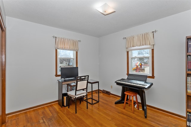 home office with visible vents, a textured ceiling, baseboards, and hardwood / wood-style flooring