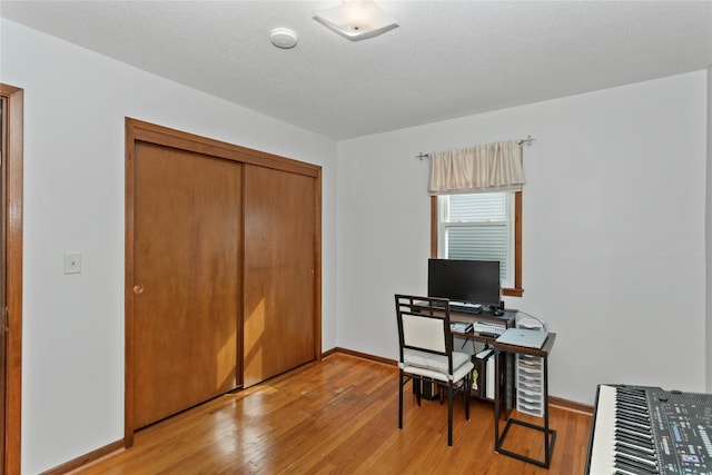 office area with light wood-style flooring, baseboards, and a textured ceiling