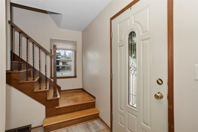 entryway with baseboards, visible vents, stairway, and wood finished floors