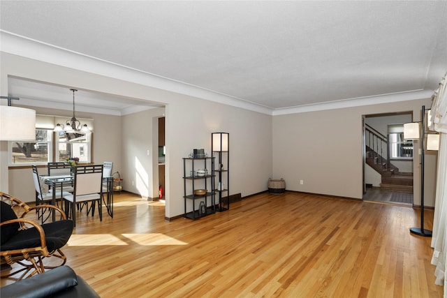 living area with baseboards, stairway, ornamental molding, light wood-style floors, and a notable chandelier