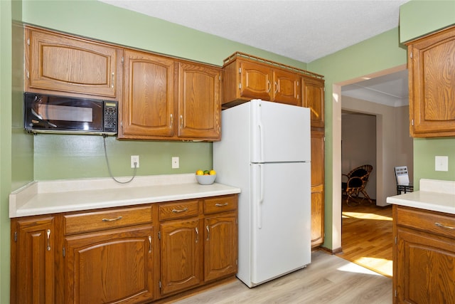 kitchen featuring brown cabinetry, light wood-style flooring, freestanding refrigerator, light countertops, and black microwave