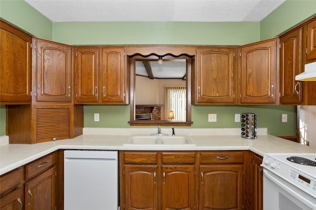 kitchen featuring white appliances, brown cabinetry, light countertops, a textured ceiling, and a sink