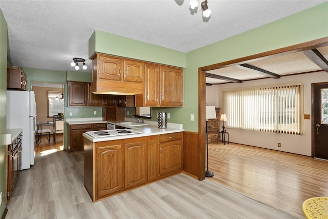 kitchen with light countertops, light wood-style flooring, a textured ceiling, white appliances, and a peninsula