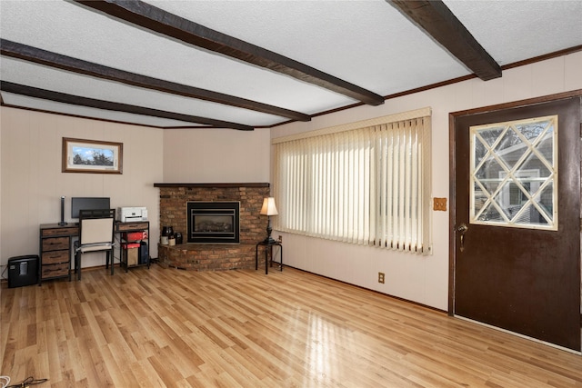 living area with a textured ceiling, beamed ceiling, a fireplace, and light wood-style floors