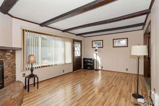 living area with light wood-type flooring, a brick fireplace, a textured ceiling, and beam ceiling