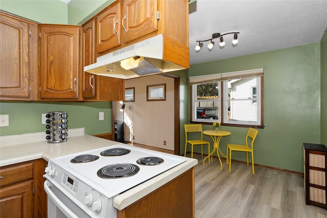 kitchen with brown cabinets, under cabinet range hood, light wood finished floors, and white electric range