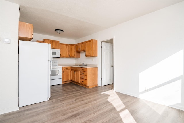 kitchen featuring white appliances, light countertops, a textured ceiling, light wood-style floors, and a sink