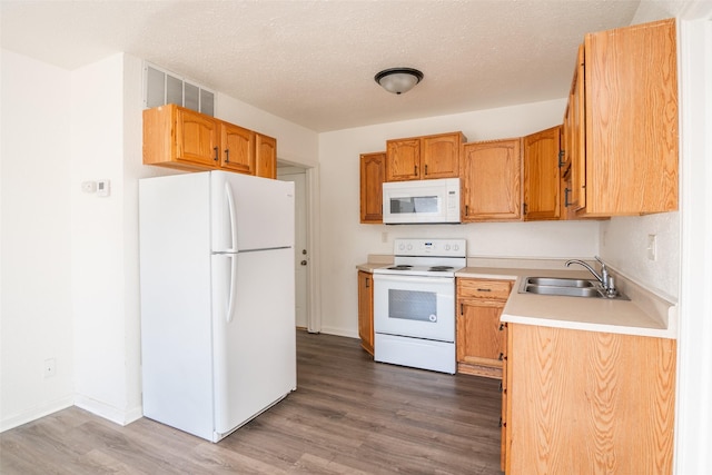 kitchen featuring white appliances, wood finished floors, light countertops, a textured ceiling, and a sink