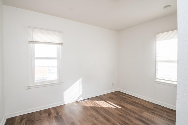 unfurnished room with baseboards, visible vents, and dark wood-type flooring