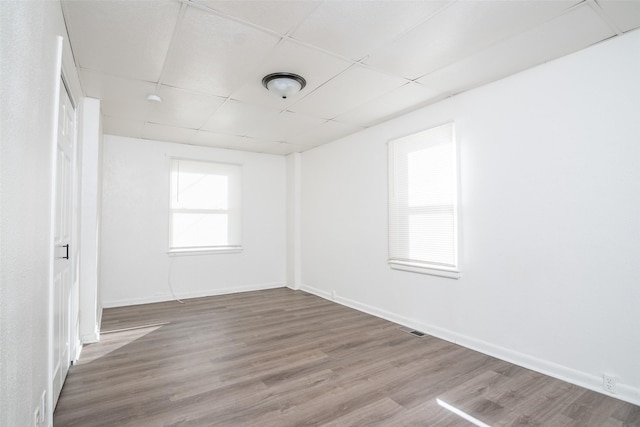 spare room with baseboards, visible vents, a drop ceiling, and wood finished floors