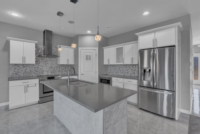 kitchen with stainless steel appliances, a kitchen island with sink, a sink, white cabinetry, and wall chimney exhaust hood