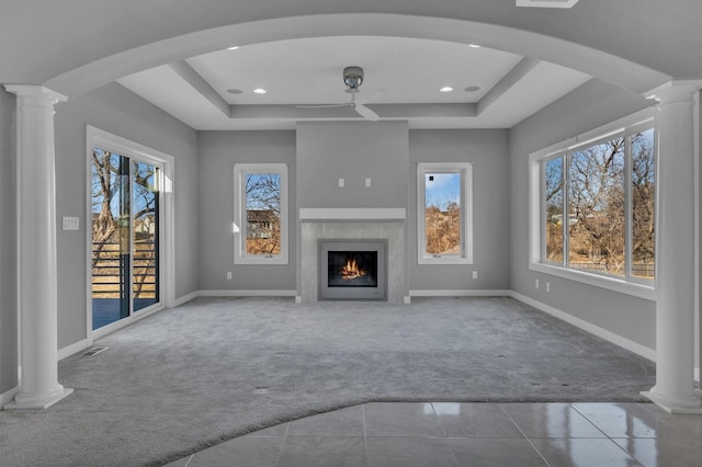 unfurnished living room with a tray ceiling, carpet flooring, decorative columns, and a healthy amount of sunlight