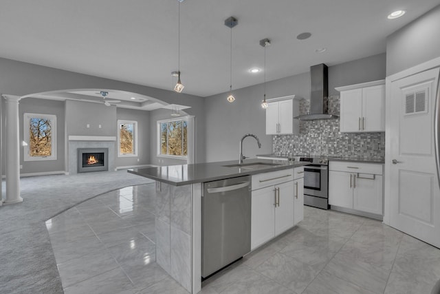 kitchen featuring a sink, white cabinetry, appliances with stainless steel finishes, wall chimney exhaust hood, and an island with sink