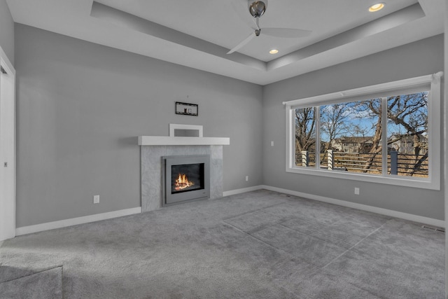 unfurnished living room featuring recessed lighting, baseboards, a lit fireplace, carpet, and a raised ceiling