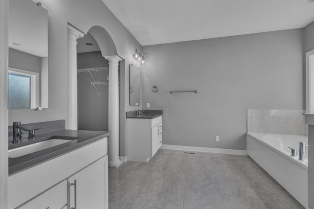 full bath with baseboards, two vanities, a sink, and ornate columns