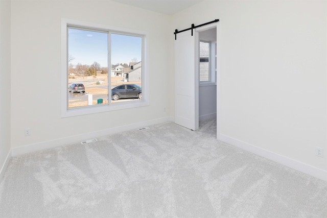 carpeted empty room with a barn door, visible vents, and baseboards