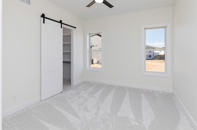 unfurnished bedroom with light carpet, a barn door, visible vents, and baseboards