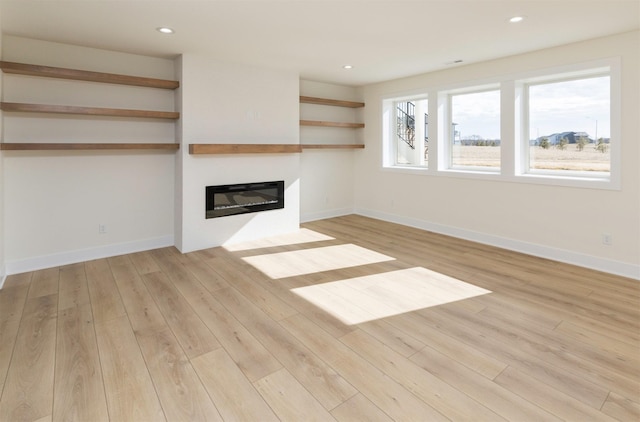 unfurnished living room with light wood-type flooring, recessed lighting, baseboards, and a glass covered fireplace