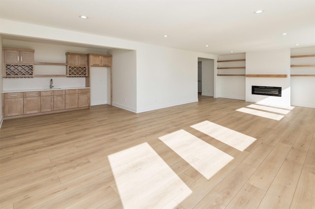 unfurnished living room with a glass covered fireplace, light wood-type flooring, a sink, and recessed lighting