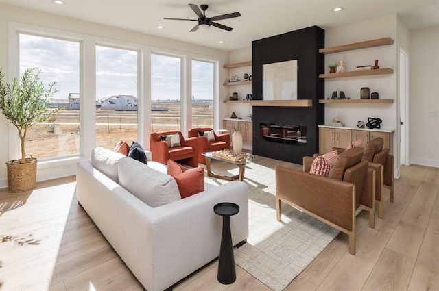 living room featuring light wood finished floors, recessed lighting, a ceiling fan, and a glass covered fireplace