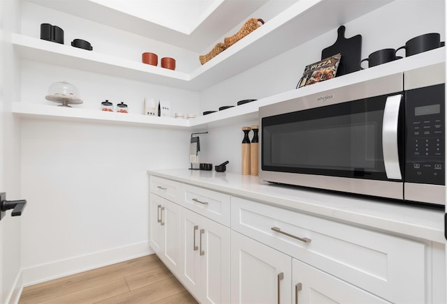 interior space featuring light wood-style flooring, white cabinetry, light countertops, open shelves, and stainless steel microwave