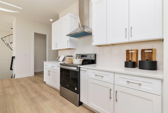 kitchen with stainless steel electric range oven, light countertops, wall chimney range hood, and light wood-style floors