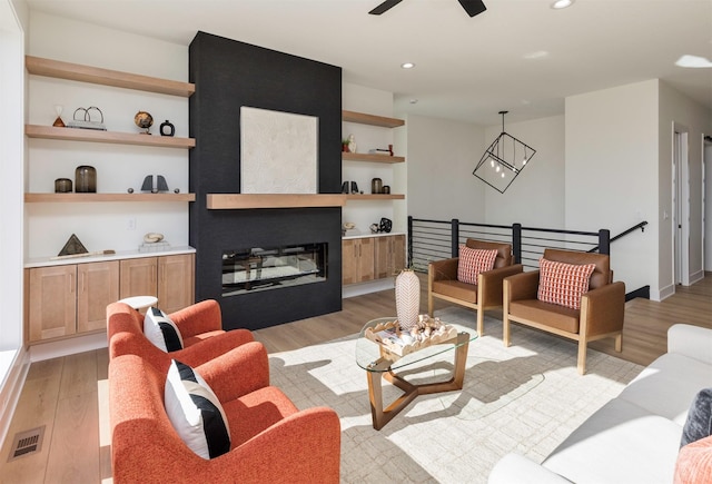 living area with visible vents, built in features, a glass covered fireplace, light wood-type flooring, and recessed lighting