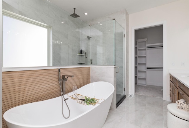 bathroom with marble finish floor, a soaking tub, a spacious closet, a stall shower, and vanity