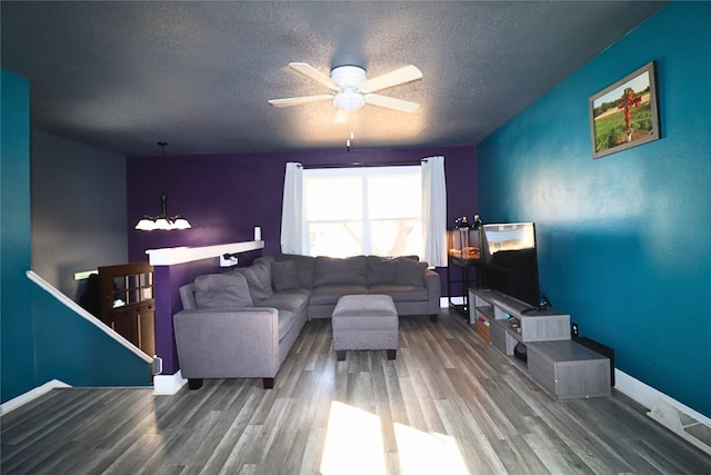 living area featuring a textured ceiling, ceiling fan with notable chandelier, wood finished floors, and baseboards