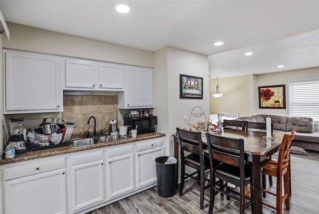 kitchen with black microwave, light wood finished floors, a sink, and tasteful backsplash