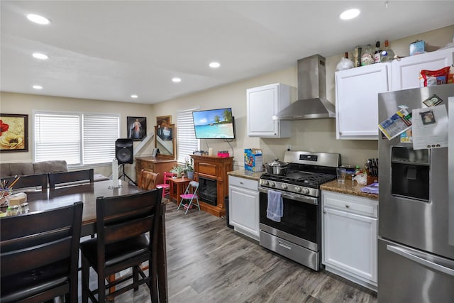 kitchen with dark wood-style flooring, recessed lighting, appliances with stainless steel finishes, white cabinets, and wall chimney range hood